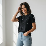 Woman wearing a black t-shirt with white heart patterns and light blue jeans indoors.