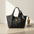 Black handbag with a gold clasp on a light surface with a vase and books in the background