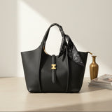 Black handbag with a gold clasp on a light surface with a vase and books in the background