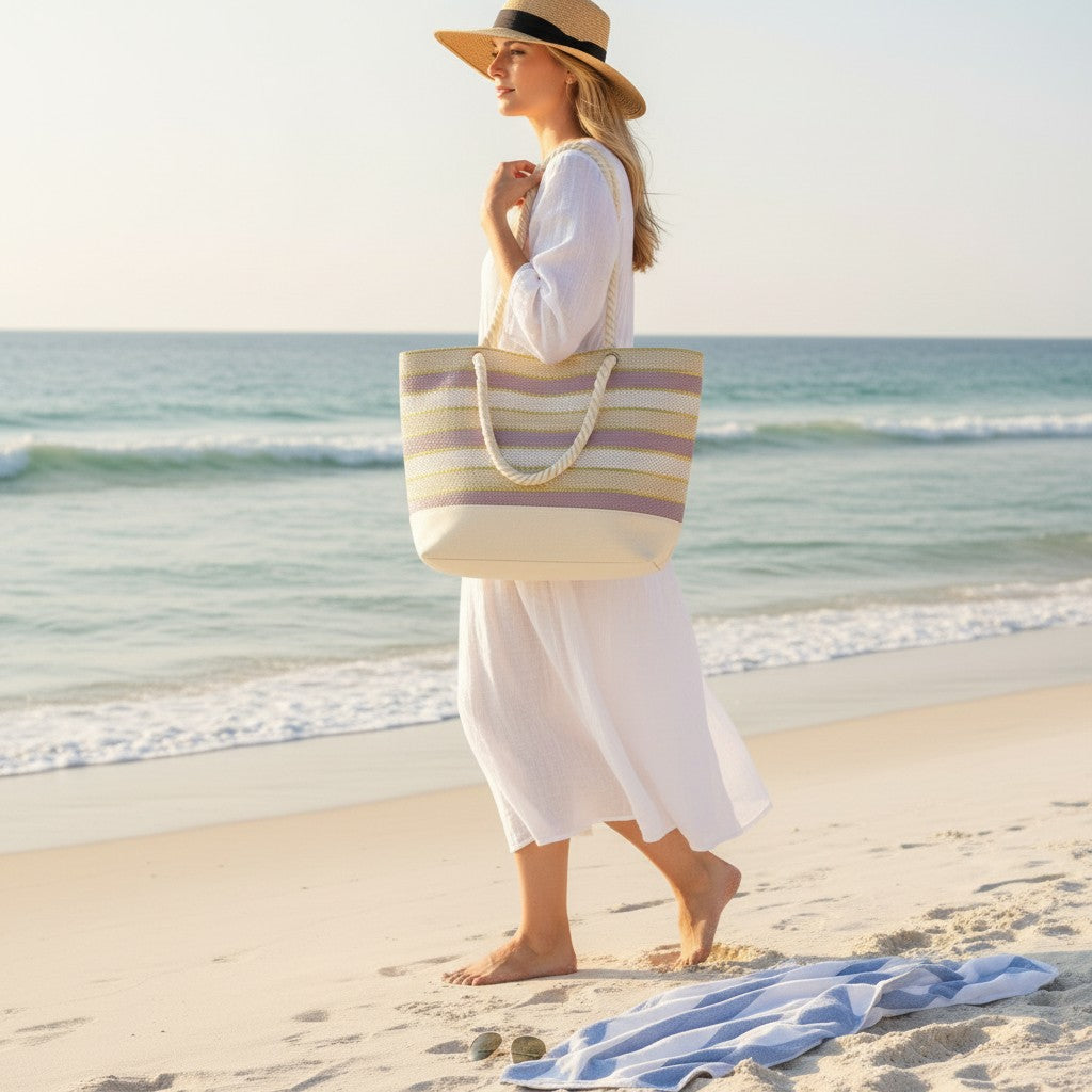 Woman on a beach holding a striped tote bag with ocean in the background
