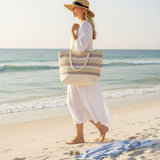 Woman on a beach holding a striped tote bag with ocean in the background
