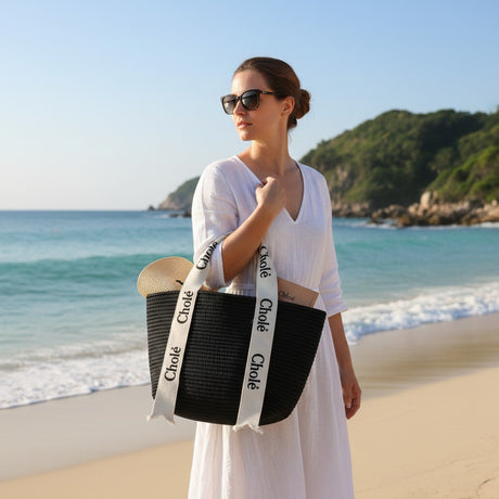 Woman holding a black bag with 'Chloé' branding on a beach.