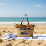 Beach bag with 'Summer Vibes' text on a sandy beach with ocean view
