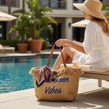 Woman sitting by a pool with a straw bag labeled 'Summer Vibes' in a sunlit outdoor setting.