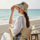 Woman at the beach wearing a straw hat and bag with palm tree designs.