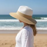 Woman wearing a white hat and dress on a beach with ocean view