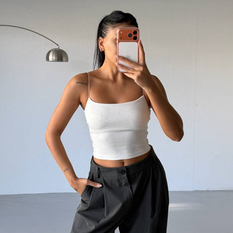 Person wearing a white tank top and black pants taking a mirror selfie.