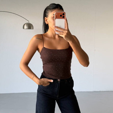 Person wearing a brown top and dark pants taking a mirror selfie against a plain background