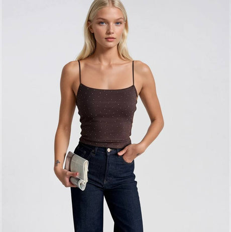 Woman wearing a brown tank top and dark blue jeans holding a clutch on a white background