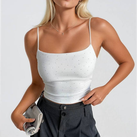 Woman wearing a white tank top and dark pants against a light background