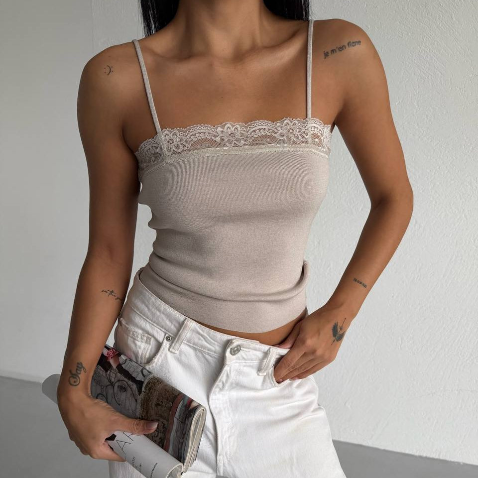 Person wearing a beige lace-trimmed top and white pants, holding a magazine.
