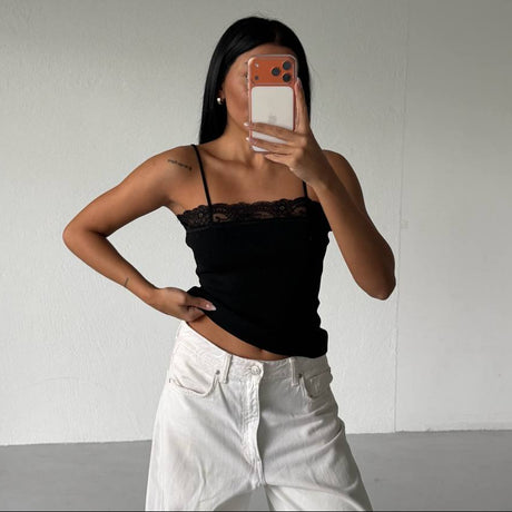 Person wearing a black top and white pants taking a mirror selfie against a plain background