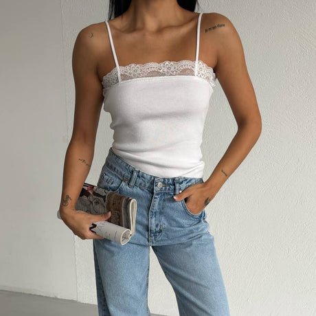 Person wearing a white lace top and blue jeans holding a clutch against a plain background