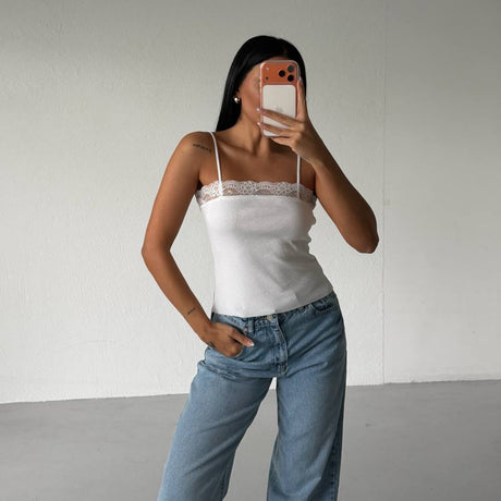 Person wearing a white top and blue jeans taking a mirror selfie against a plain background