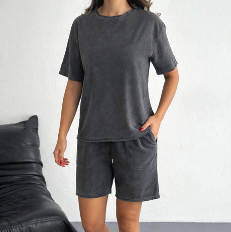 Person wearing a gray t-shirt and shorts set with white sneakers in a minimalistic setting.