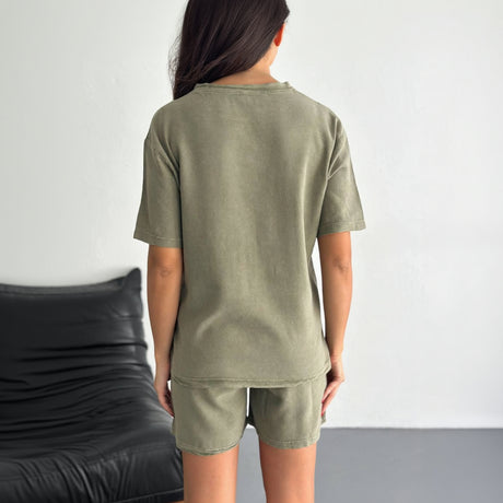 Person wearing an olive green t-shirt and shorts set against a neutral background.