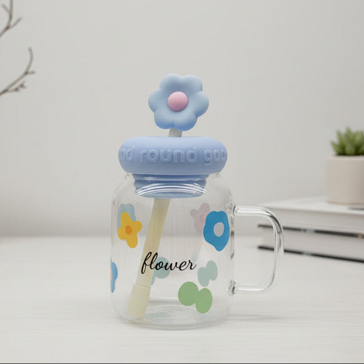 Glass mug with floral design and blue lid on a white surface with minimal background