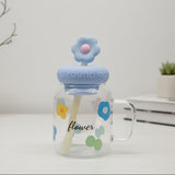 Glass mug with floral design and blue lid on a white surface with minimal background