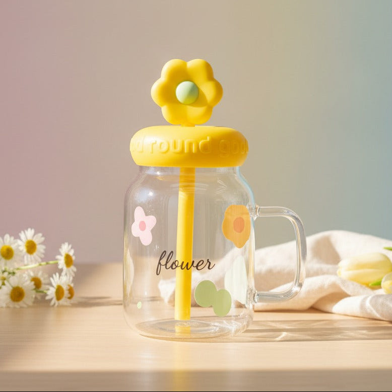 Clear mug with yellow flower lid and straw on a wooden surface with flowers and a cloth.
