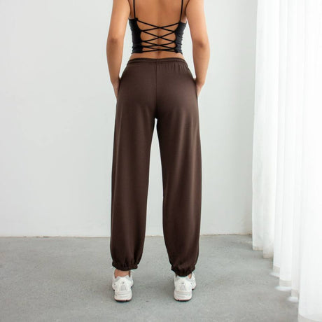 Person wearing a black strappy top and brown sweatpants against a white background