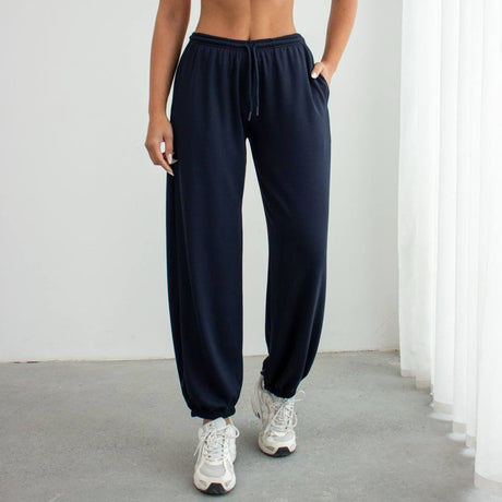 Woman wearing a white strapless top and navy sweatpants against a white background