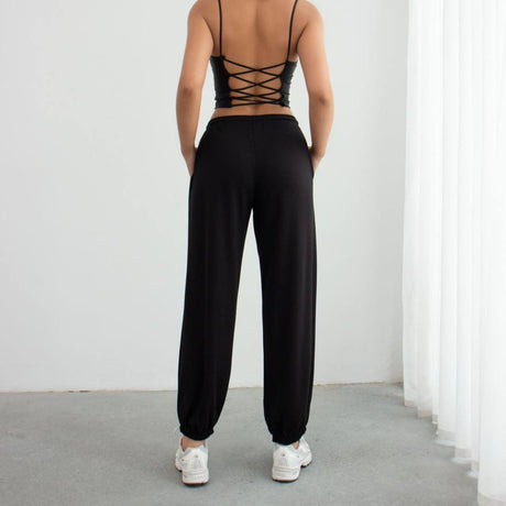 Person wearing a black strappy top and black pants against a white background