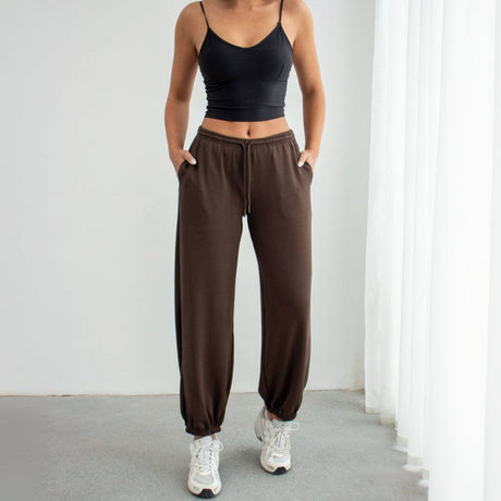 Person wearing a black crop top and brown sweatpants against a white background