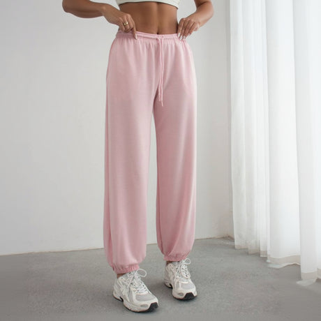 Person wearing pink sweatpants and white sneakers on a plain background