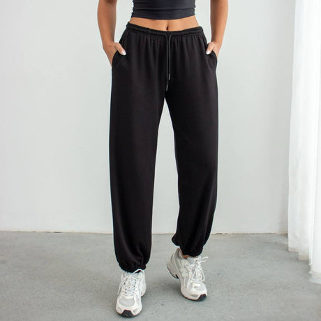 Person wearing a black athletic outfit with white sneakers on a light gray background