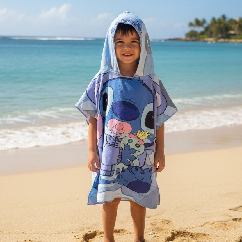 Child wearing a cartoon-themed towel on a beach with ocean and sky in the background