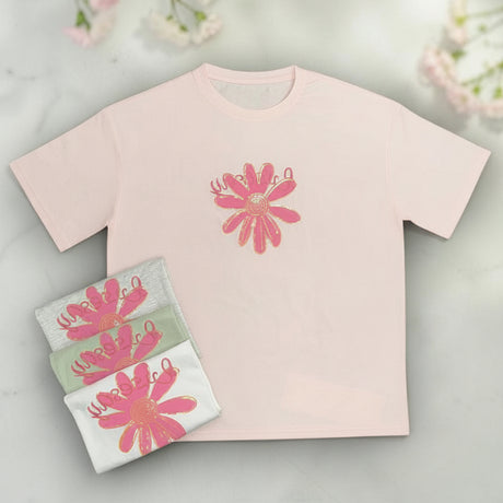 Pink t-shirt with floral design and matching pouch on a marble surface with flowers in the background