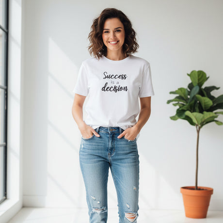 White t-shirt with 'Success is a decision' text on a dark surface with clothes and shoes in the background.