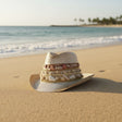 Straw hat with decorative band on a sandy beach with ocean and palm trees in the background