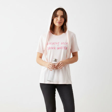 Pink Tshirt with the text "Breathe  deep drink water" worn by a woman holding a bottle with a grey bakground