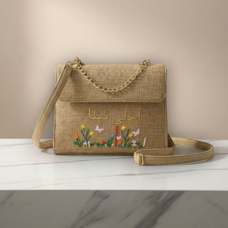 Brown textured handbag with floral embroidery and chain handle on a white surface.