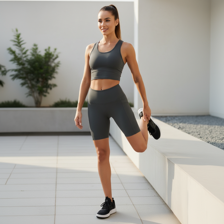 Woman in gray athletic wear stretching outdoors on a sunny day.