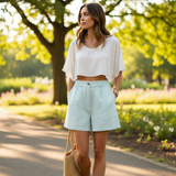 Woman in a white top and light blue shorts standing in a park.