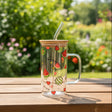Clear glass tumbler with watermelon design and wooden lid on a reflective surface.