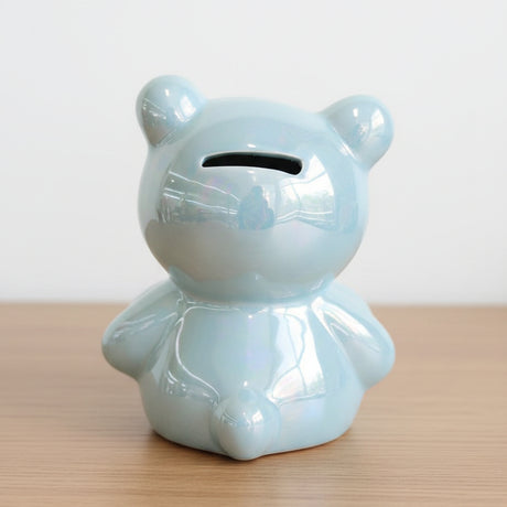 Blue ceramic bear-shaped money box on a white surface with a blurred store background.