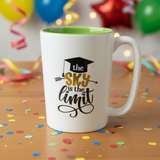 White mug with green interior, 'The sky is the limit' text, colorful confetti and balloons in the background