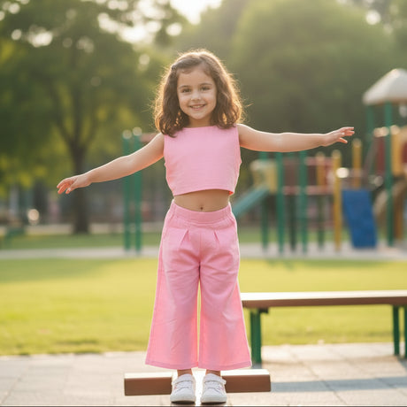 Young girl in a pink outfit standing outdoors with trees and playground equipment in the background