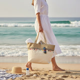 Woman in a white dress holding a beach bag on a sandy beach with ocean waves in the background