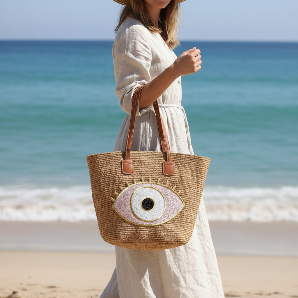 Woman holding a straw tote bag with eye design on a beach