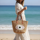 Woman holding a straw tote bag with eye design on a beach