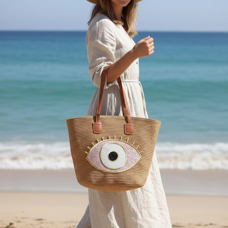 Woman holding a straw tote bag with eye design on a beach