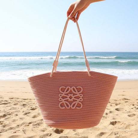 Woven beach bag held by a hand on a sandy beach with ocean waves in the background