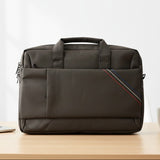 Black laptop bag on a wooden desk with a laptop, mug, and notebook in the background.
