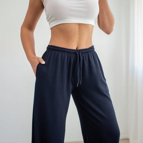 Person wearing navy sweatpants and a white crop top on a light gray background