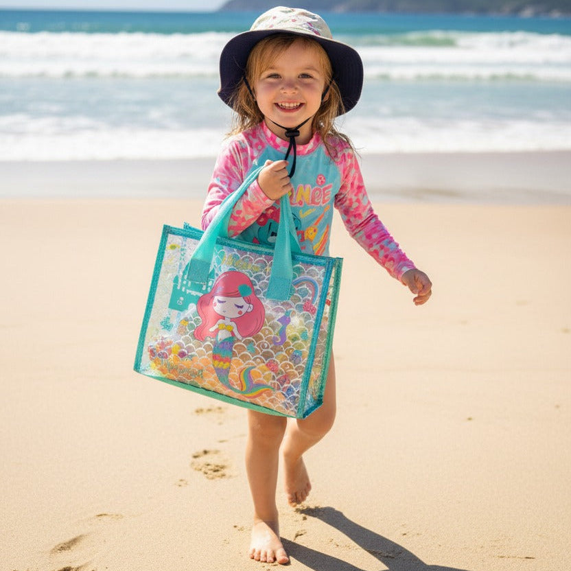 Child on a beach holding a colorful bag with a mermaid design