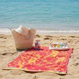 Beach scene with a colorful towel, bag, and toys on sand by the ocean